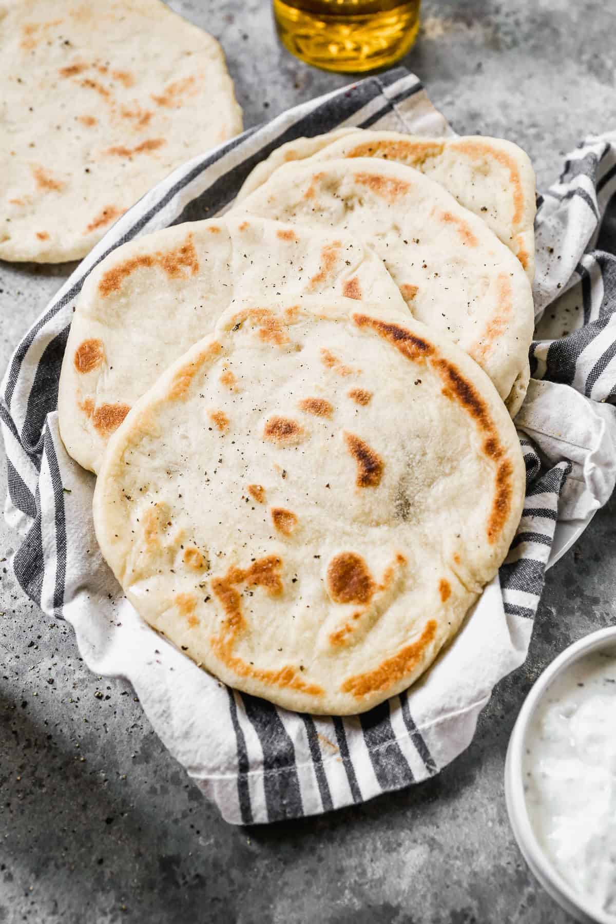 A stack of homemade pita bread on a dish towel, freshly cooked and ready to eat. 