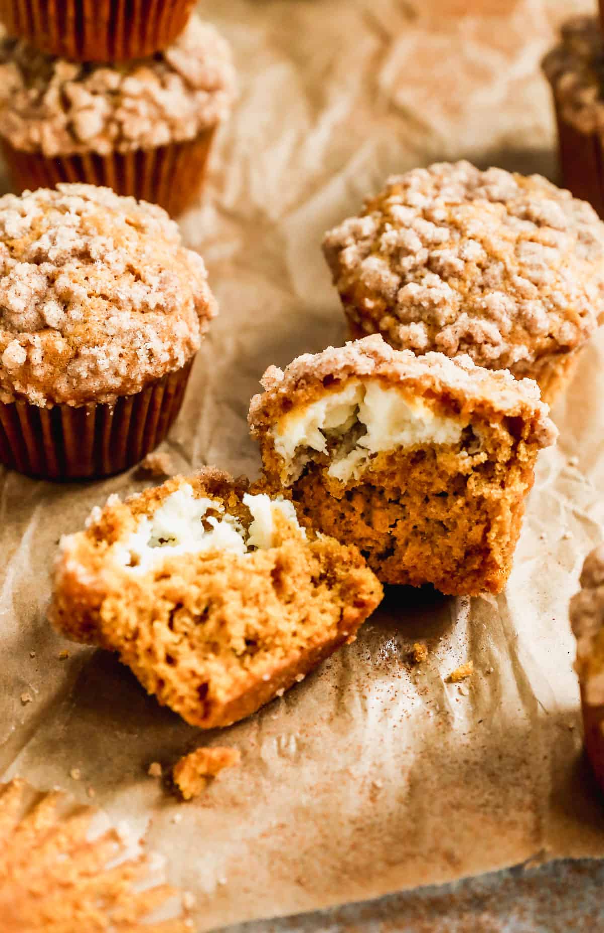 A close up image of a pumpkin cream cheese muffin sliced in half to show the baked cream cheese filling. 
