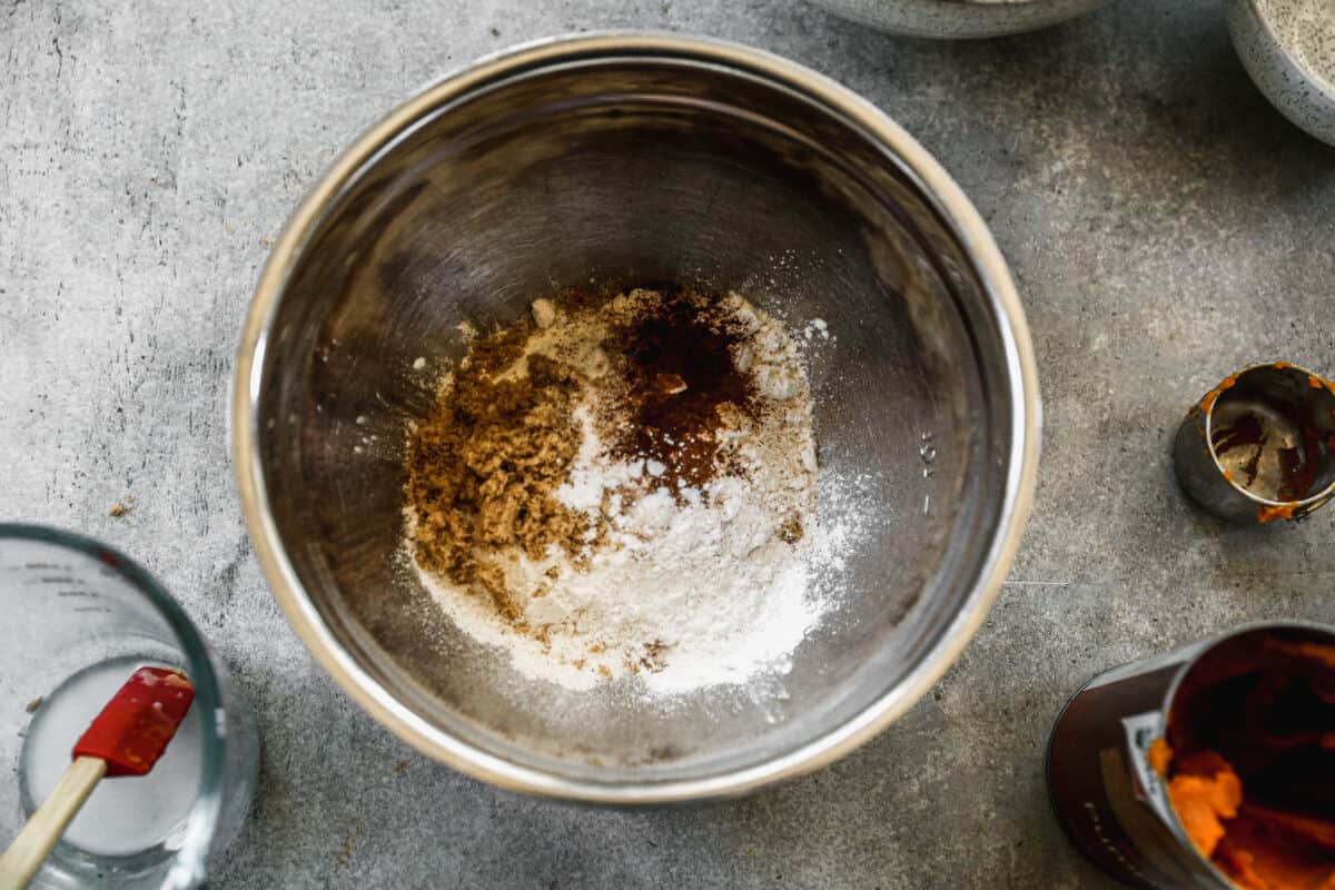 Flour, brown sugar, baking powder, baking soda, allspice, cinnamon, and salt in a stainless steel mixing bowl.