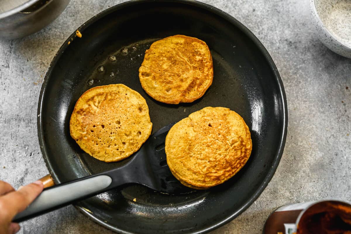 Three small easy pumpkin pancakes cooking in a pan.