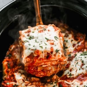 A piece of easy crockpot lasagna being lifted from the slow cooker by a spatula.