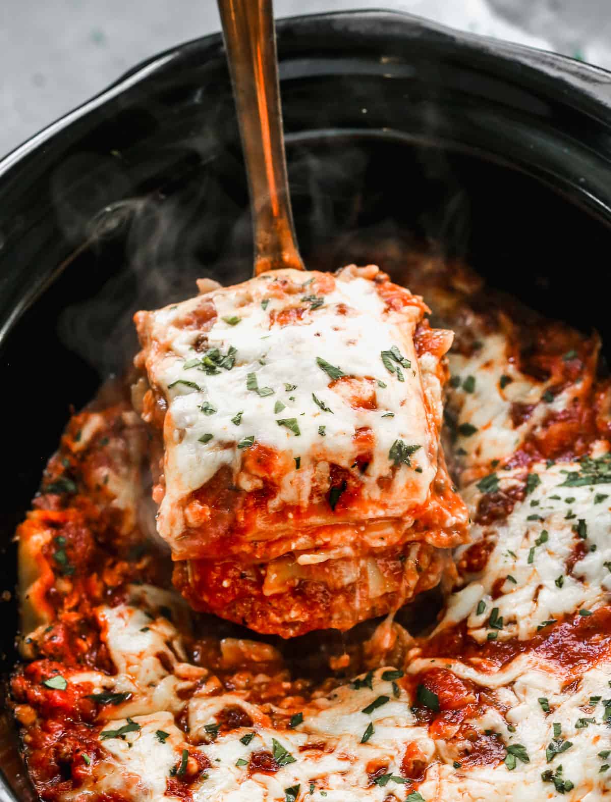 A piece of homemade slow cooker lasagna being lifted from a slow cooker with a spatula.