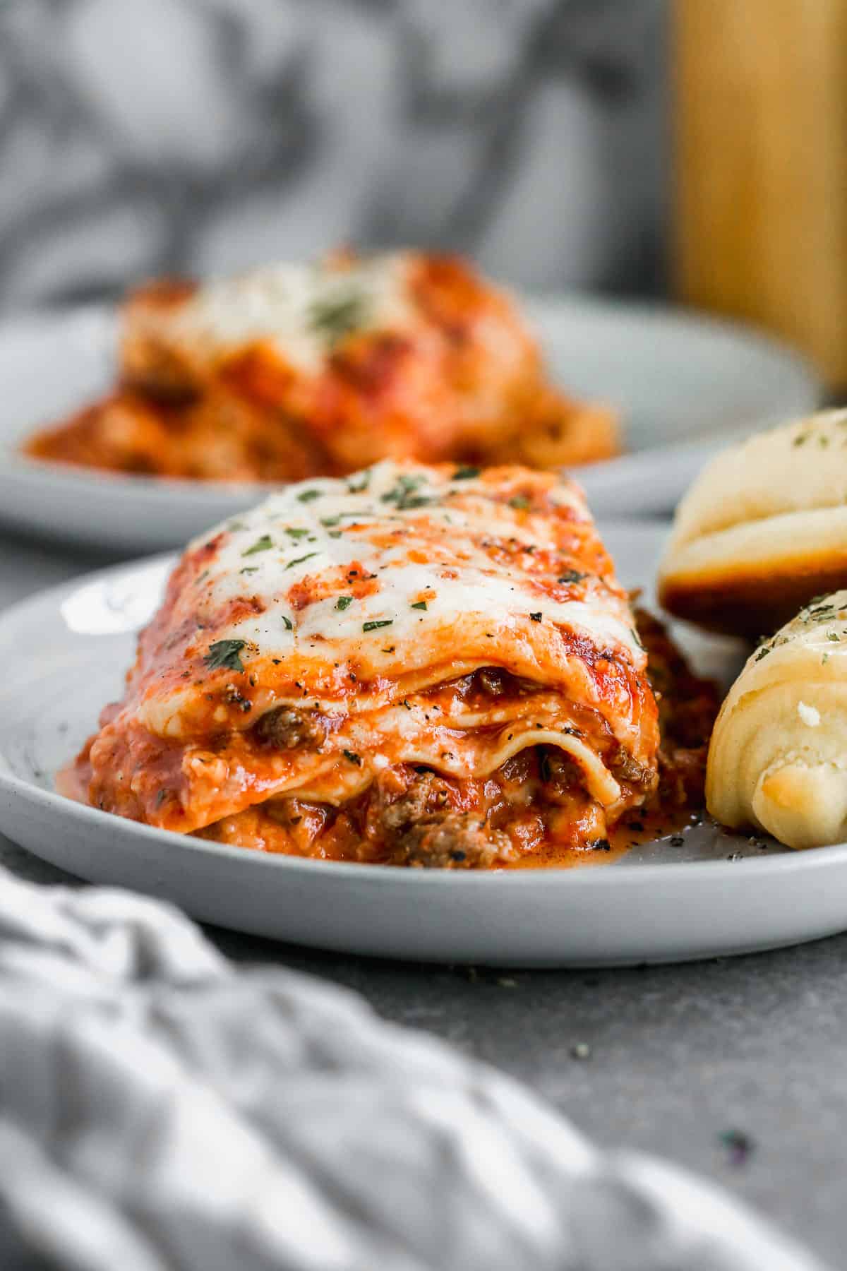 A piece of an easy slow cooker lasagna recipe on a white plate with some garlic knots, ready to enjoy.