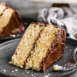 A slice of a moist yellow cake with chocolate frosting on a plate with a fork.
