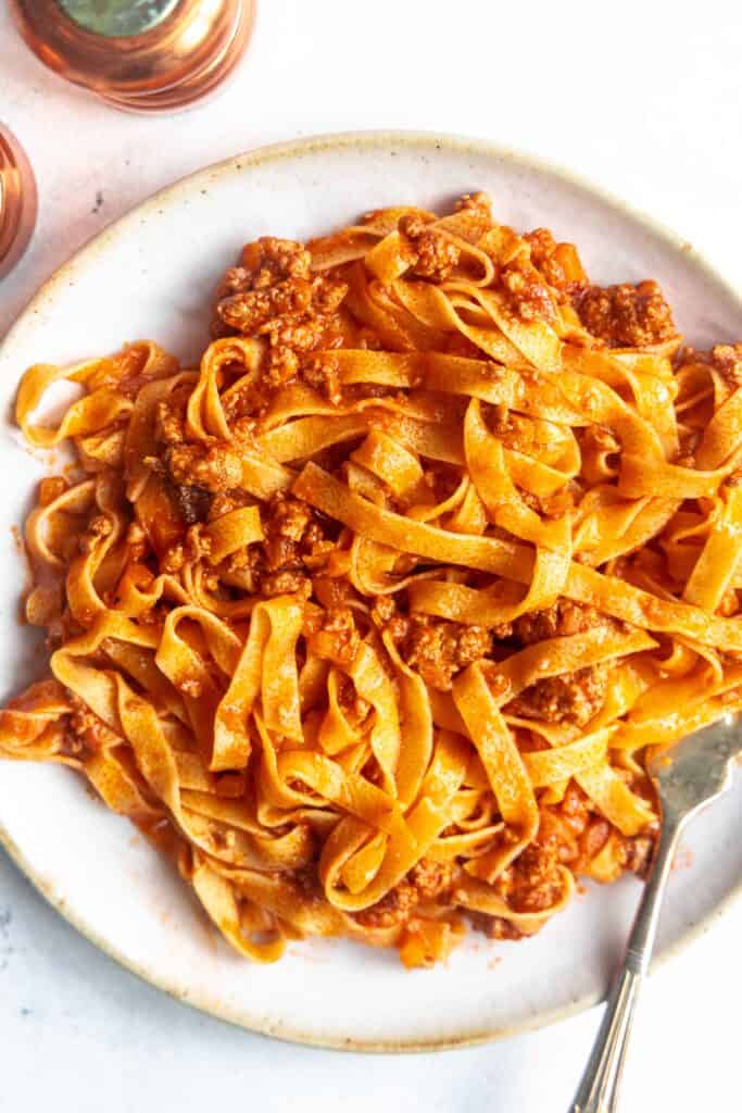 Bolognese Ragu over fresh egg pasta on a white plate, ready to enjoy.