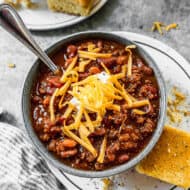 A bowl of the best classic chili recipe, topped with cheese and sour cream and a side of cornbread.