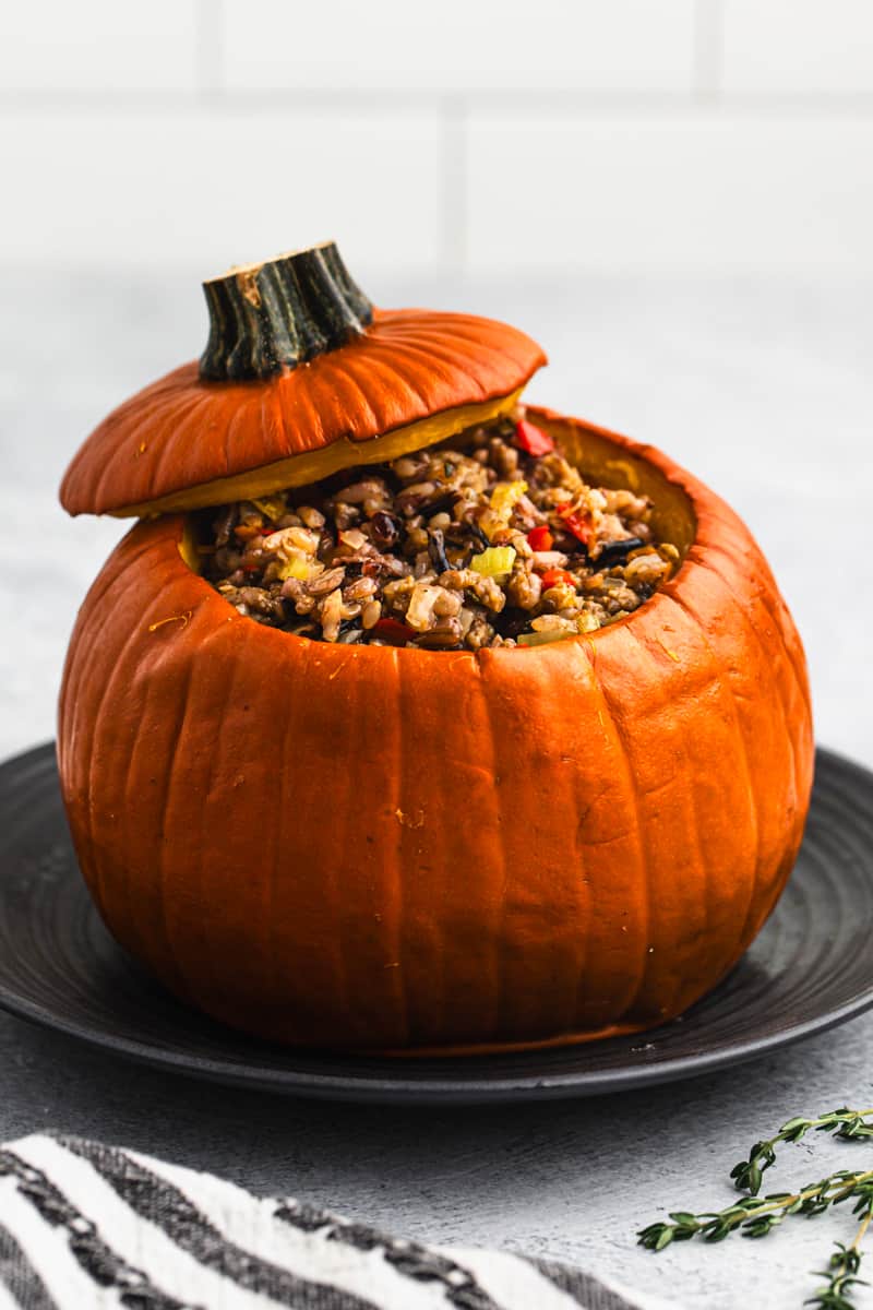 A festive Dinner in a Pumpkin made of wild rice, sausage, and veggies inside a pie pumpkin on a plate.