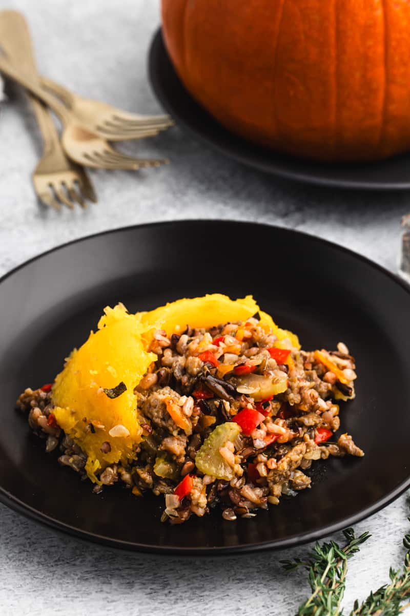 An easy dinner in a pumpkin made of wild rice, sausage, and vegetables scooped out and put on a plate with fresh cooked pumpkin.