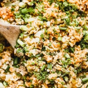 An easy dirty rice recipe packed with beef, sausage, vegetables, and a ton of bold flavors in a large pan, ready to serve with a wooden spoon.