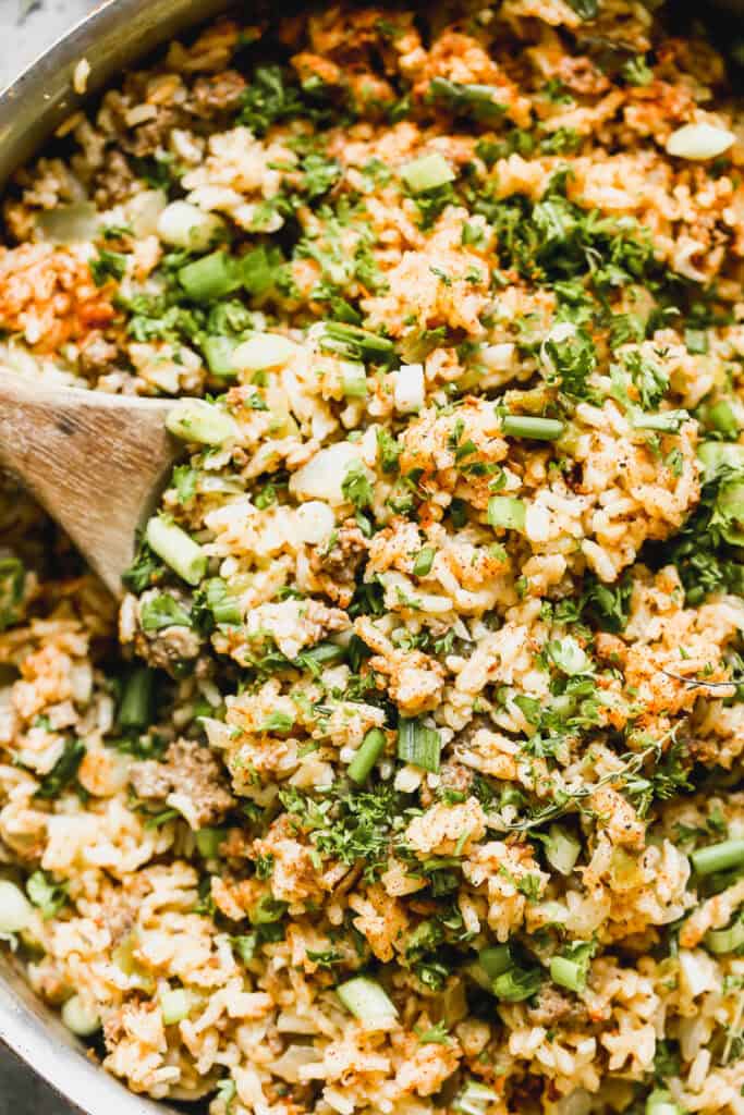 An easy dirty rice recipe packed with beef, sausage, vegetables, and a ton of bold flavors in a large pan, ready to serve with a wooden spoon.