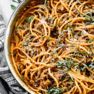 An easy Harissa Pasta recipe in a stainless steel pan, topped with freshly grated parmesan cheese and chopped basil.