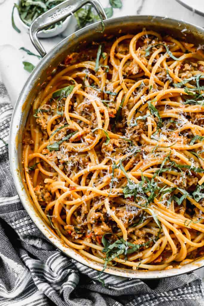 An easy Harissa Pasta recipe in a stainless steel pan, topped with freshly grated parmesan cheese and chopped basil.
