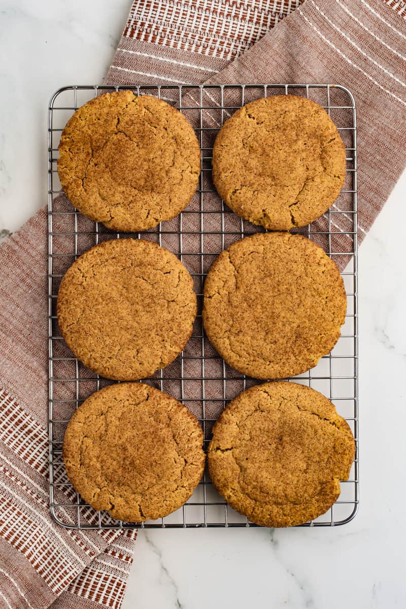 Six homemade Pumpkin Snickerdoodle cookies on a wire cooling rack.
