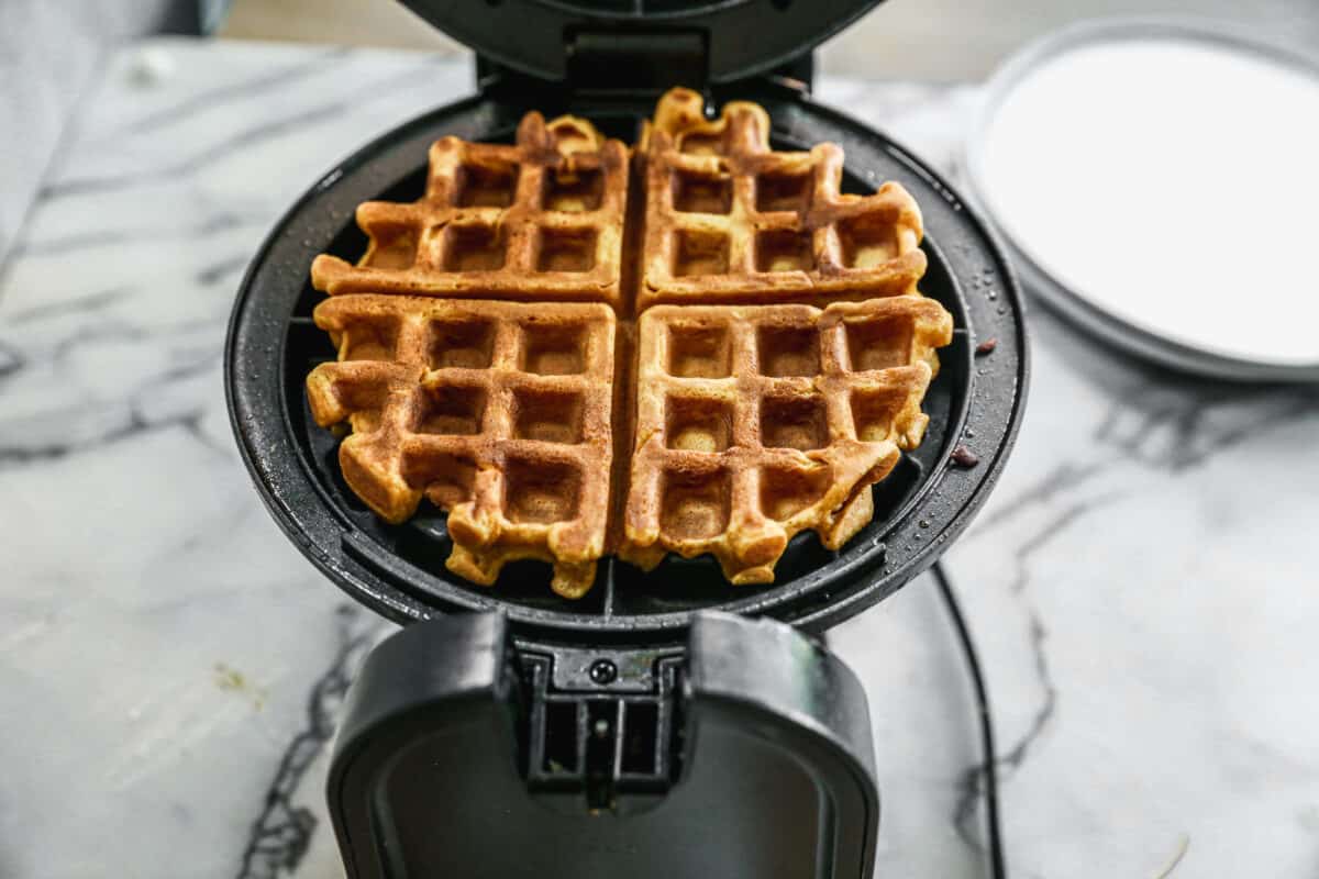 The best pumpkin waffles being cooked on a waffle iron until golden brown.