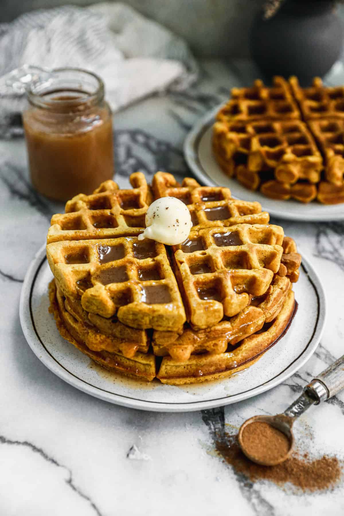 A stack of three Pumpkin Waffles on a plate topped with butter and homemade cinnamon syrup.