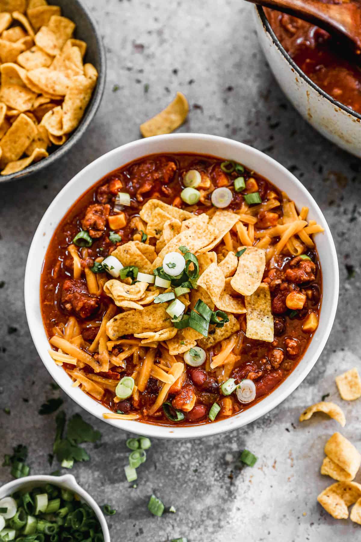 A bowl of Taco Soup topped with shredded chedar cheese, fritos, and chopped green onions. 