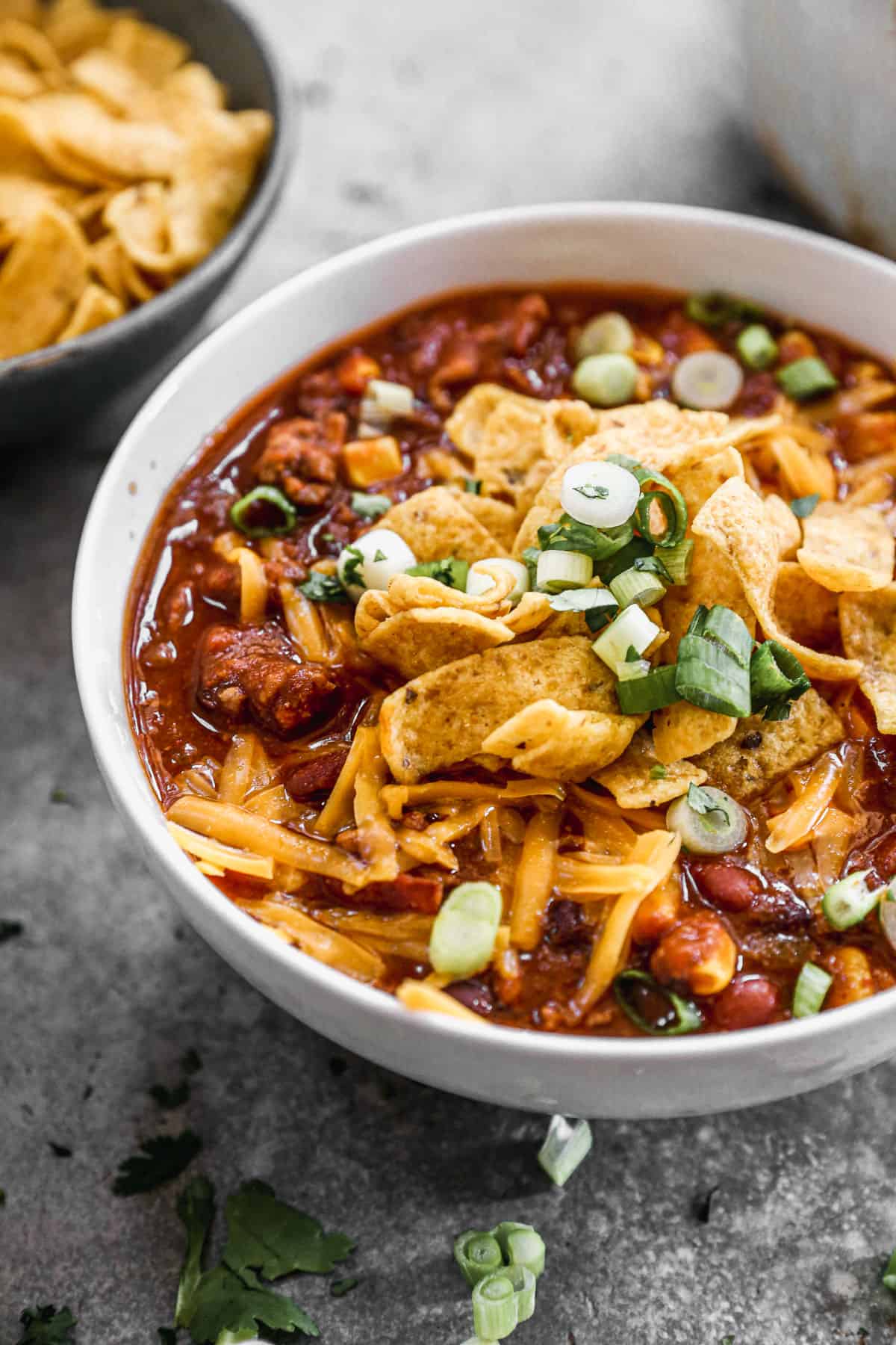 A close image of a bowl of creamy taco soup, topped with cheddar cheese, corn chips, and green onions. 