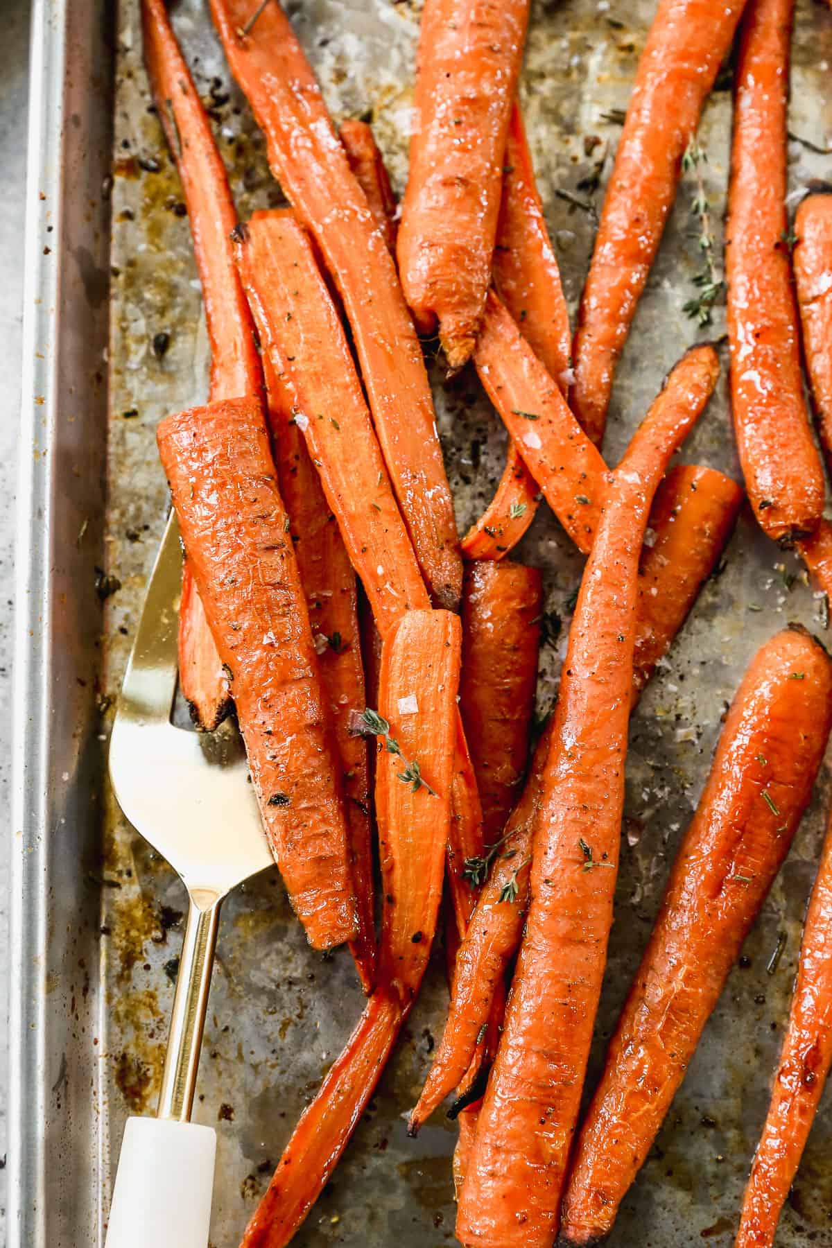 A close up image of honey Balsamic Roasted Carrots with fresh herbs, on a baking sheet.