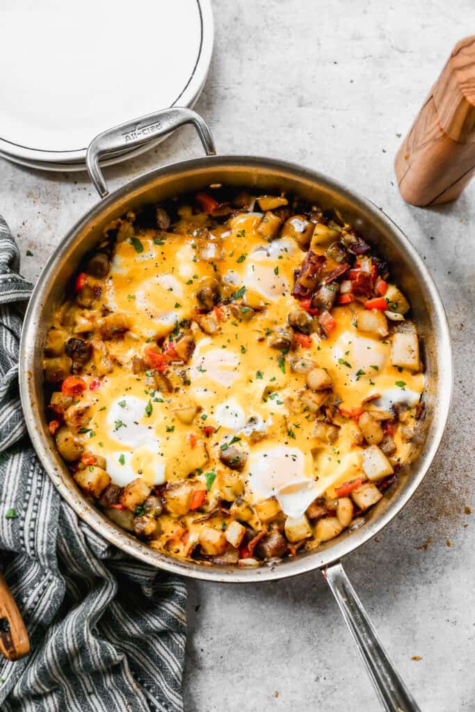 An easy Breakfast Skillet recipe in a large stainless steel pan with potatoes, eggs, bacon, sausage, and shredded cheese.