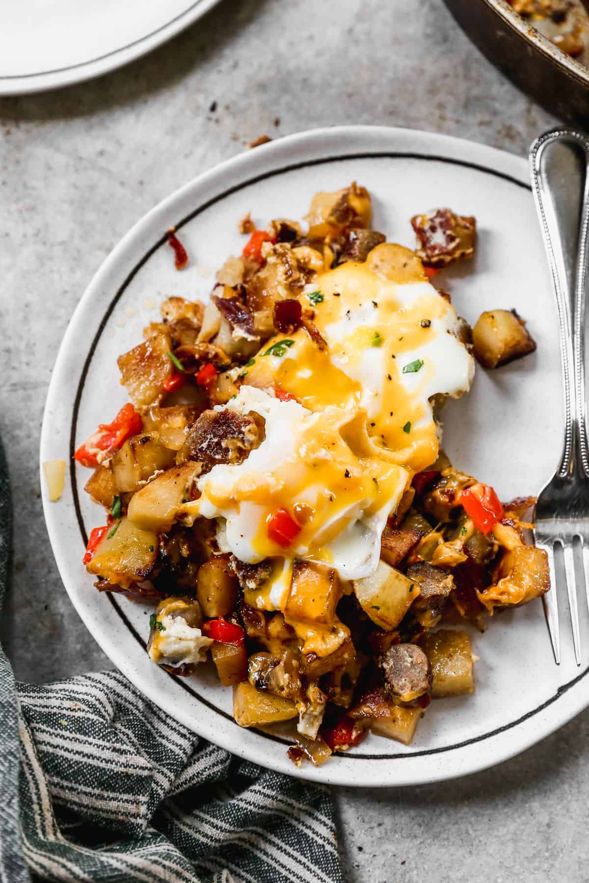 Some hearty breakfast skillet on a plate made with potatoes, bacon, sausage, peppers, onions, eggs, and cheese. 