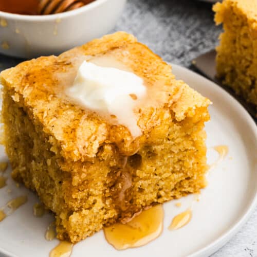 Moist buttermilk cornbread on a plate topped with butter and a drizzle of honey.