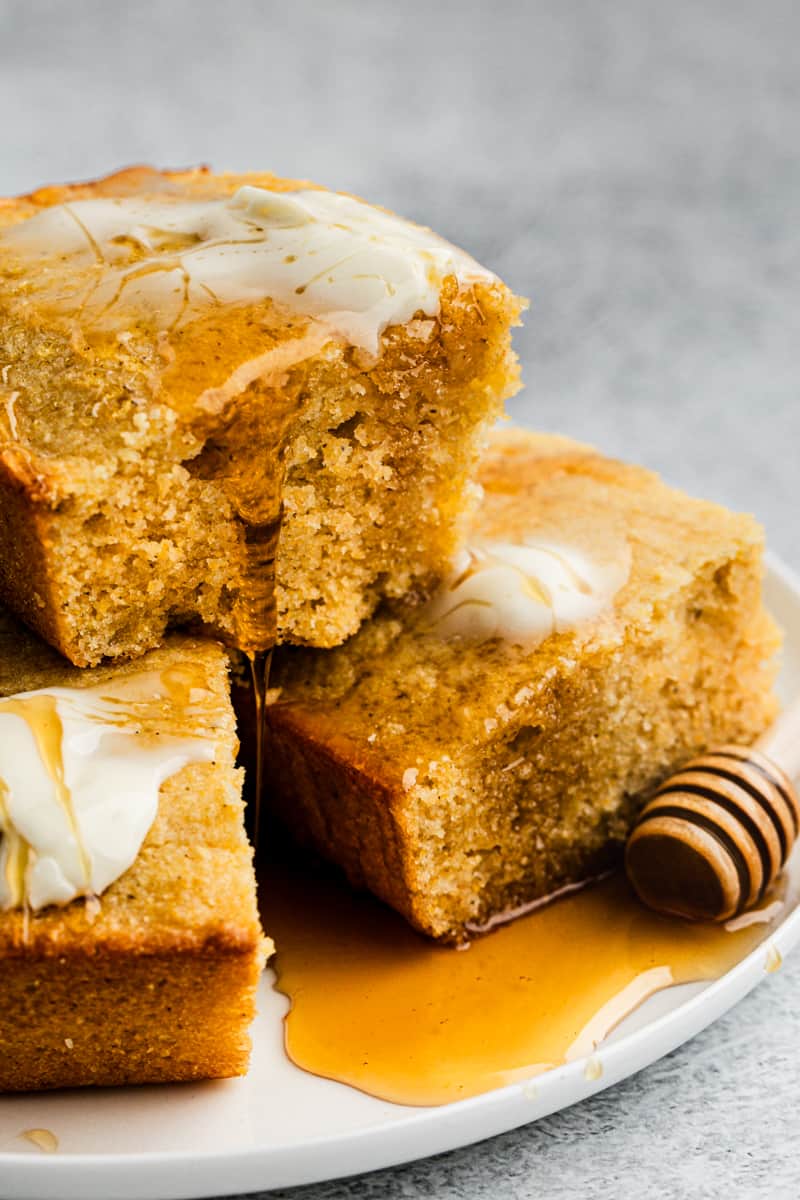 Three squares of buttermilk cornbread with one stacked on top, all topped with butter and honey.
