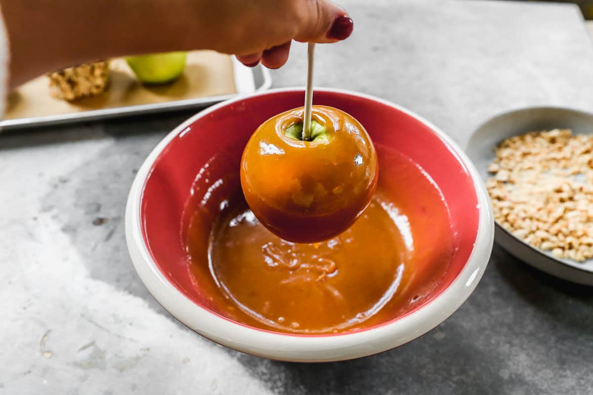A caramel apple being lifted from a bowl of caramel after being dipped.
