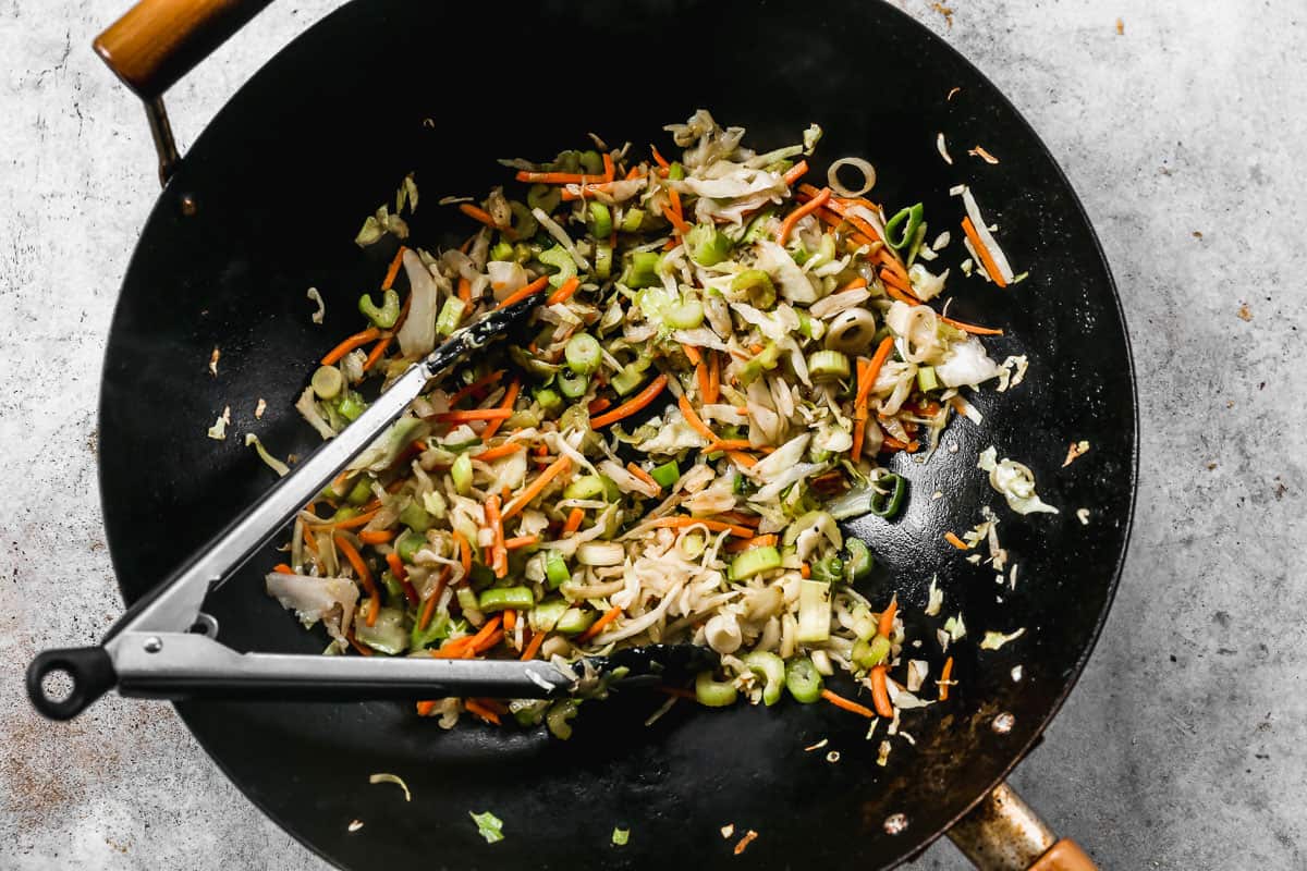 Shredded cabbage, carrots, celery, and green onion being sautéed in a wok for homemade Chow Mein.