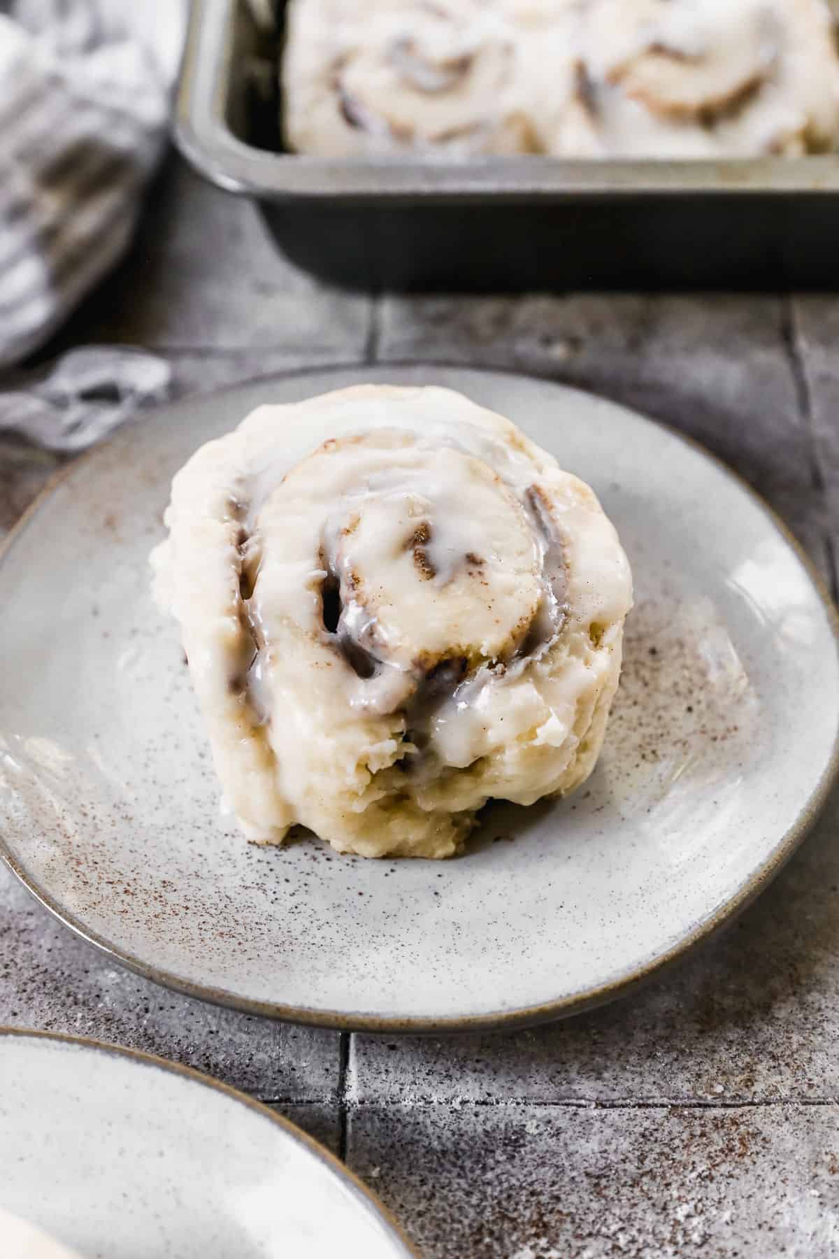 A homemade Cinnamon Roll Biscuit on a white plate, covered in a simple glaze.