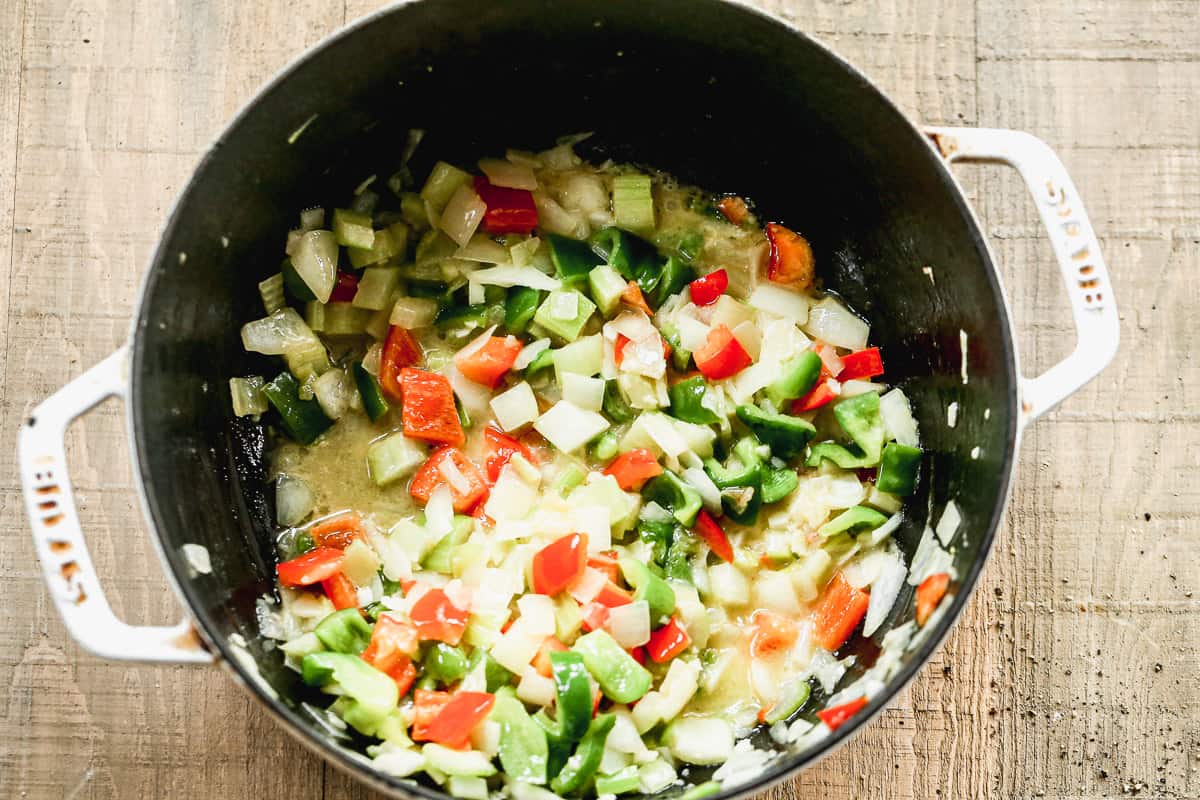 A large pot filled with chopped onions, celery, bell peppers, and garlic being sautéed in olive oil and butter.
