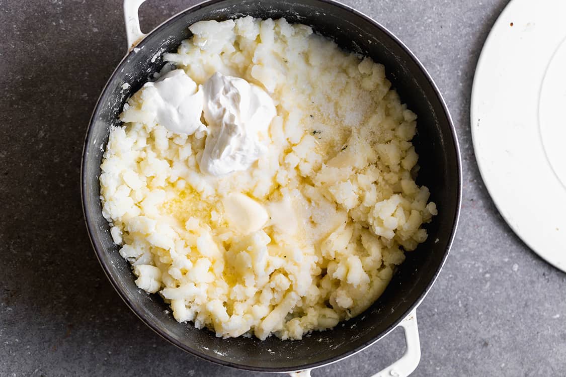 A pot of homemade mashed potatoes with sour cream and butter on top, ready to be mixed.