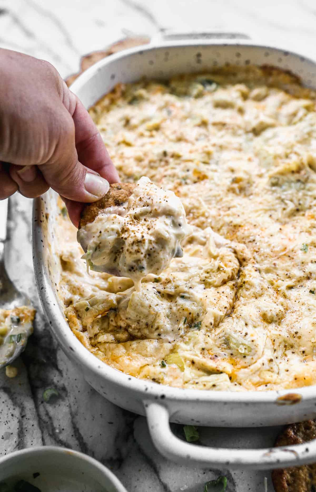 Someone scooping up homemade Crab Artichoke Dip on a cracker.