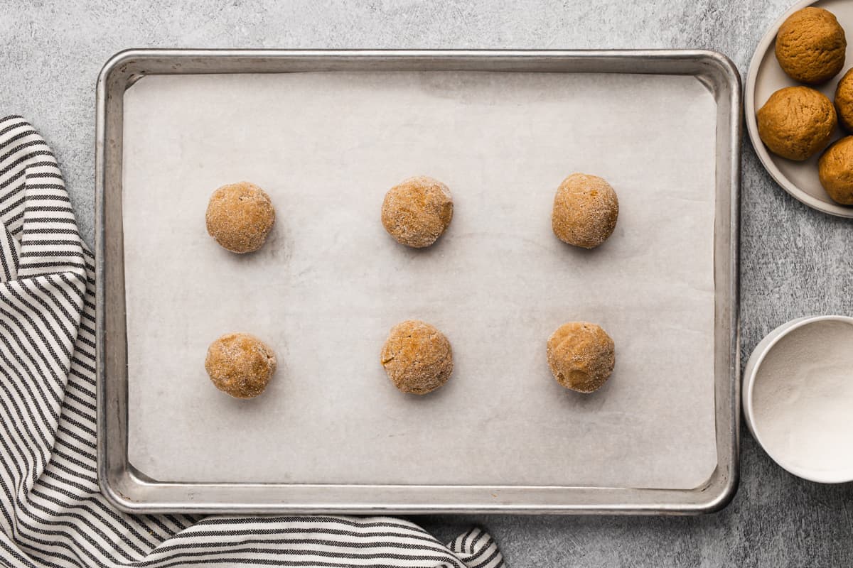 Six Ginger Molasses cookie dough balls on a baking sheet, after being rolled in sugar.