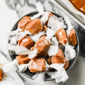 A bowl of easy Homemade Caramels, wrapped in parchment paper pieces.