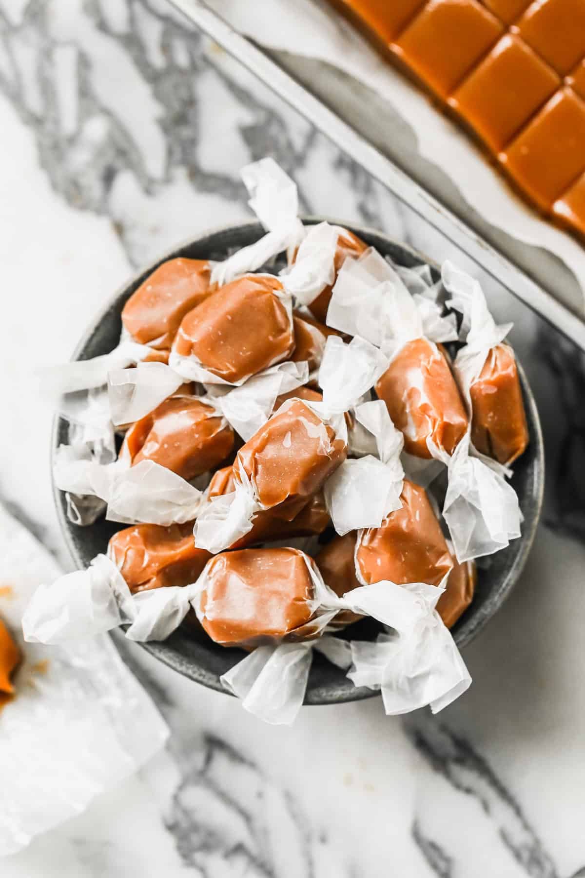 A bowl of easy Homemade Caramels, wrapped in parchment paper pieces.