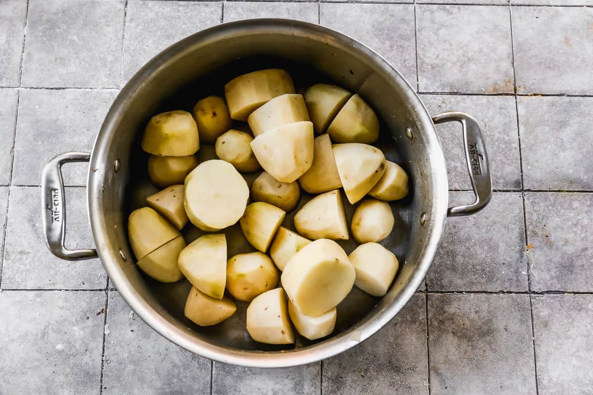 A pot with peeled potatoes, chopped in half.
