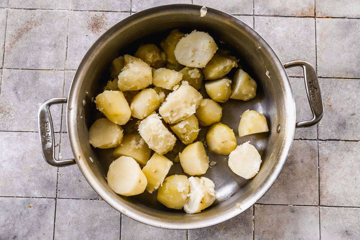 A pot with chunks of cooked potatoes, steaming, to make an easy Mashed Potatoes recipe.