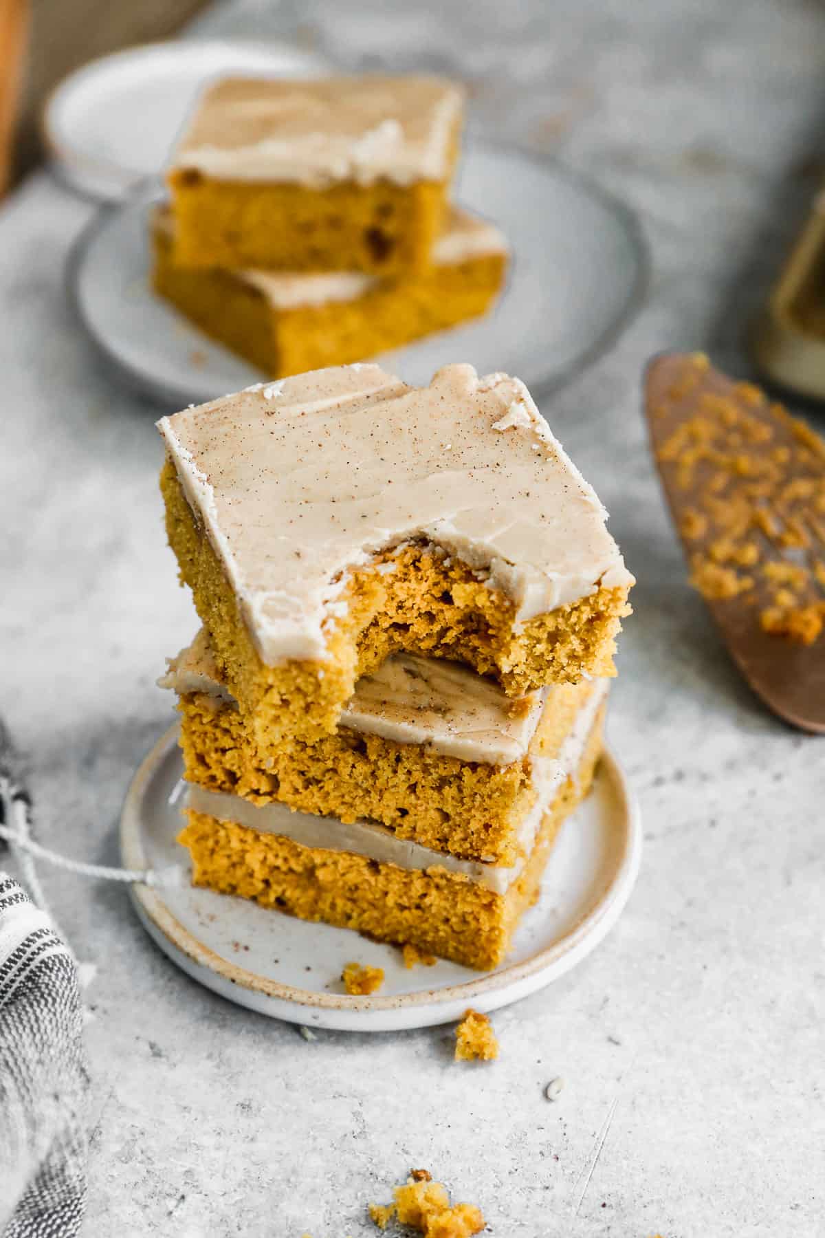 Three frosted Pumpkin Bars with caramel frosting stacked on top of each other with a bite taken out of the top one.
