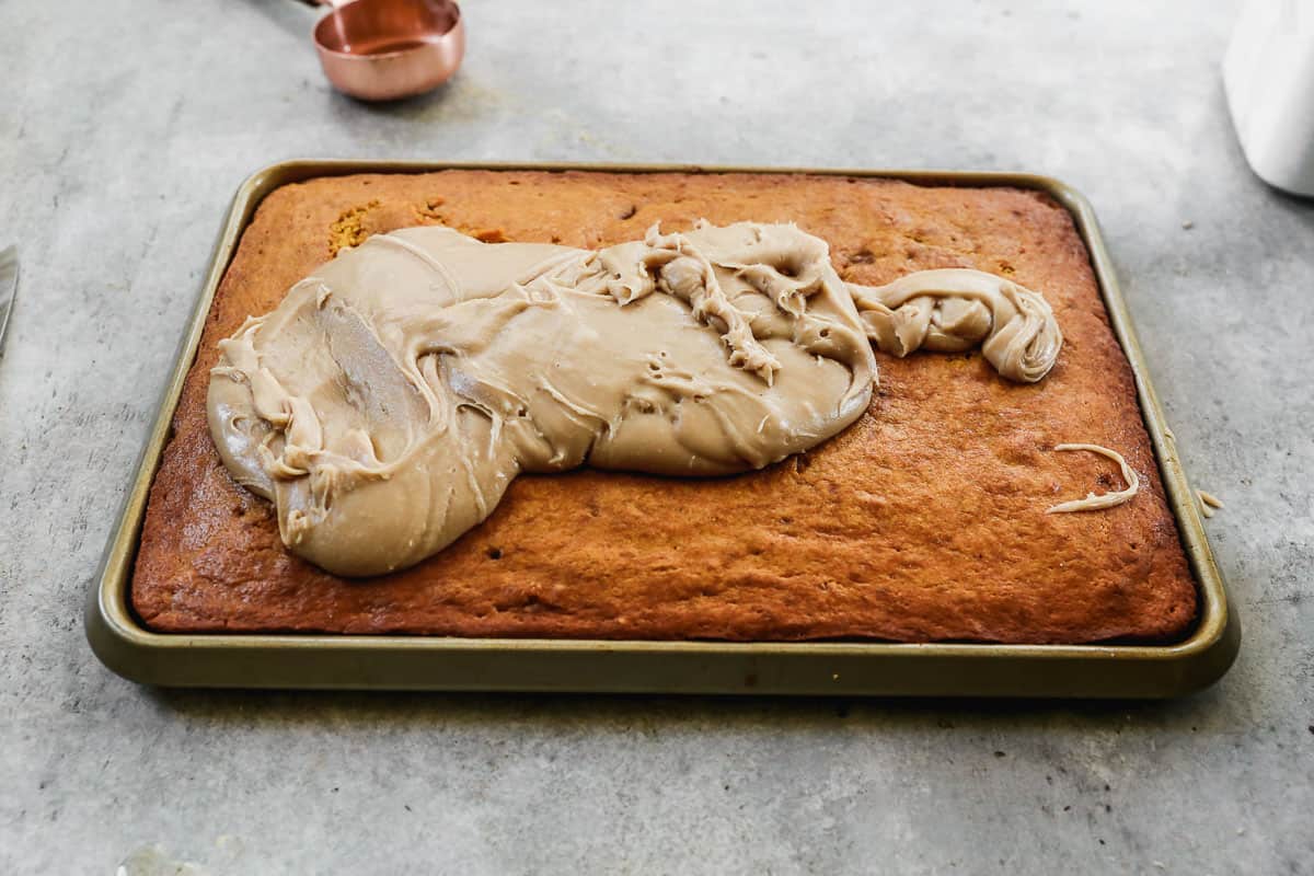 Warm pumpkin bars in a baking sheet with a pile of homemade caramel frosting dumped on top.