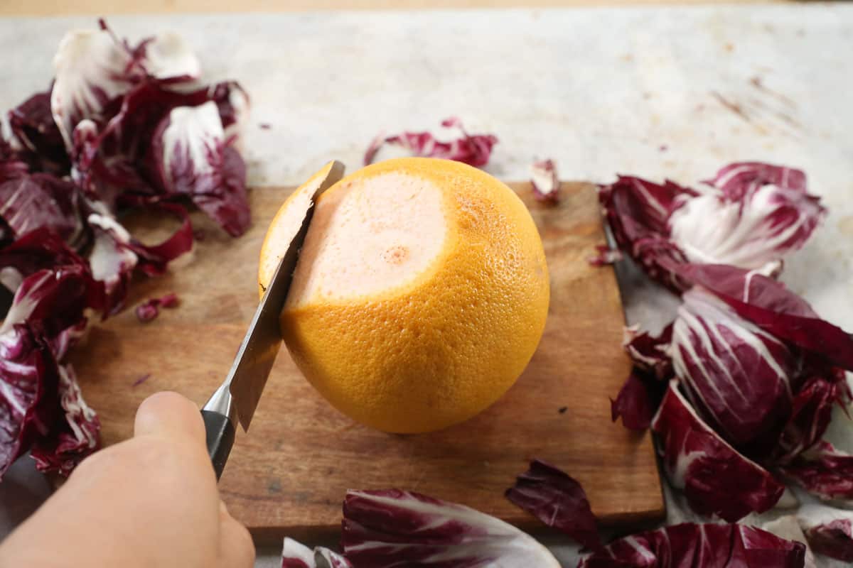 A grapefruit being peeled with a knife to be used in a salad.