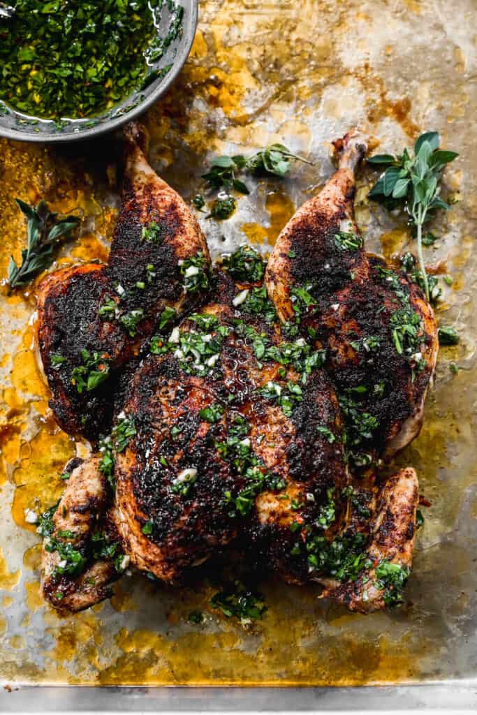 A whole Spatchcock Chicken on a piece of parchment paper fresh out of the oven, covered in a dry rub and chimichurri sauce.