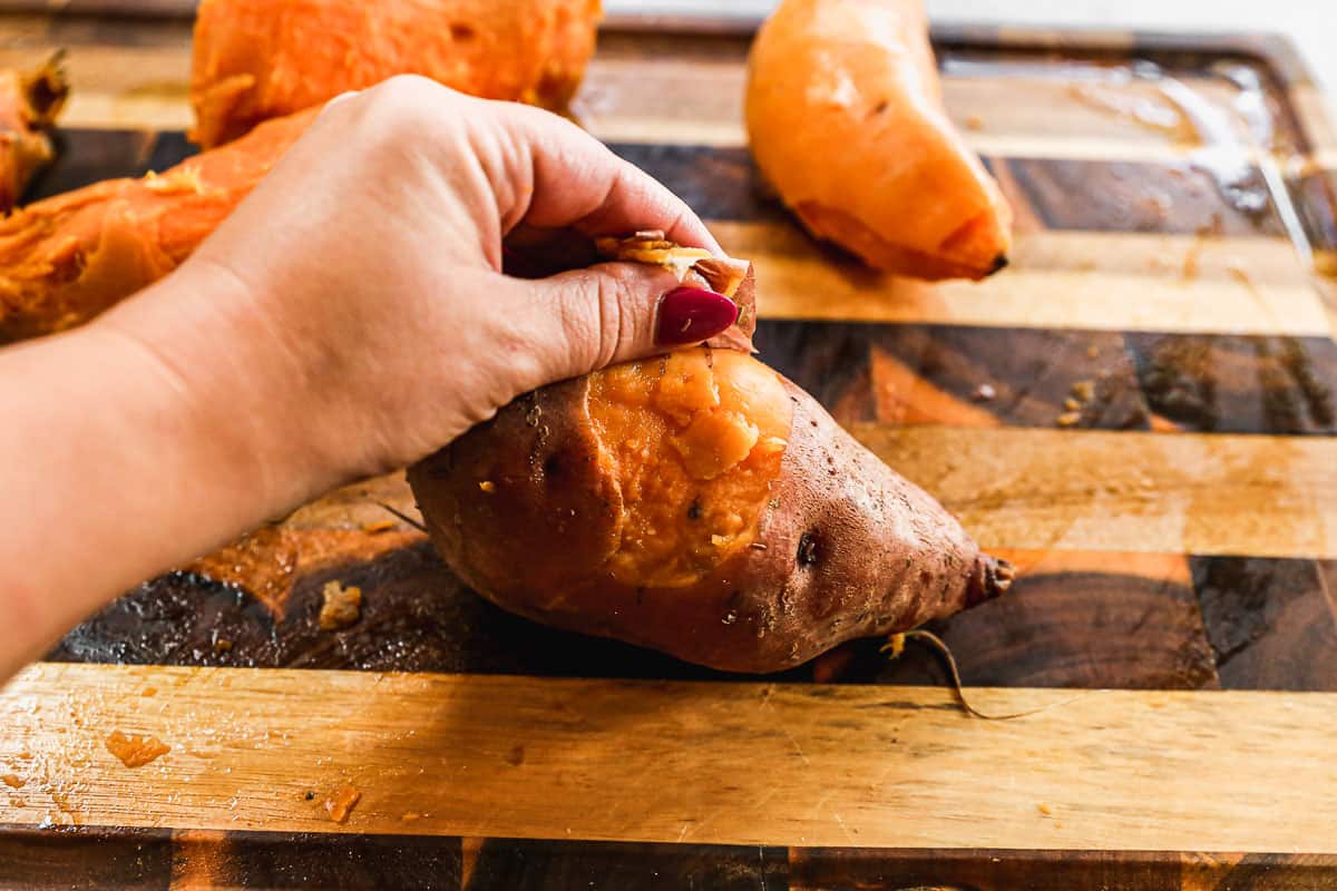 Someone peeling the skins off of sweet potatoes on a cutting board.