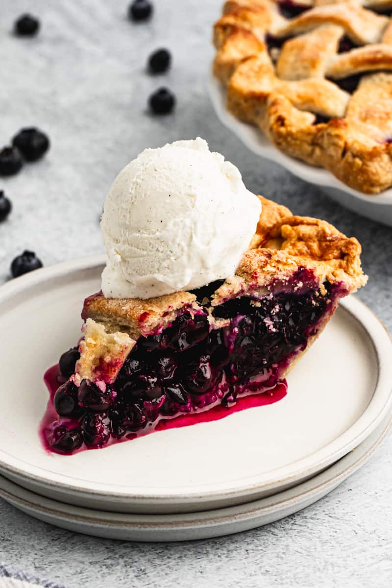 A slice of homemade Blueberry Pie on a plate, topped with vanilla bean ice cream.