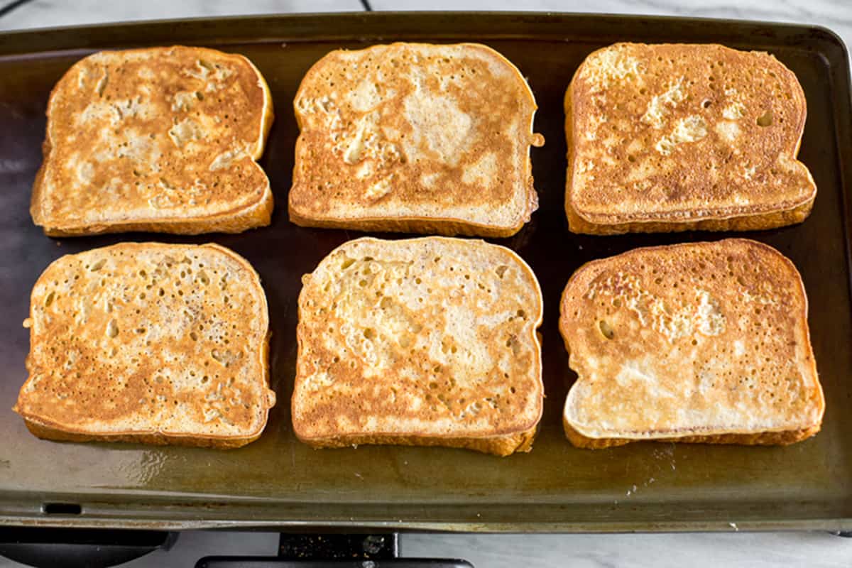 Homemade brioche french toast recipe on a griddle, cooked golden brown.