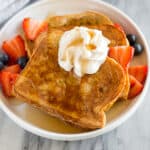 The best Brioche French Toast recipe, stacked and topped with whipped cream and a side of berries.
