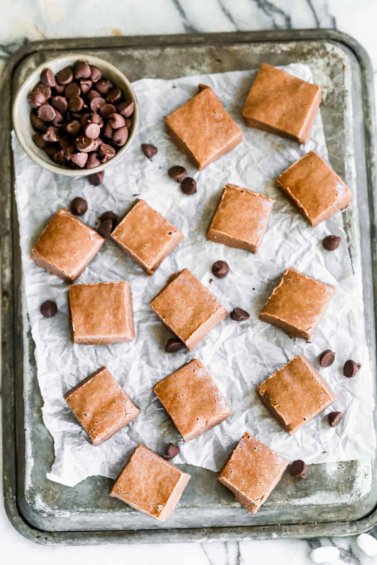 A simple fudge recipe, cut into squares on a piece of parchment paper, garnished with chocolate chips.
