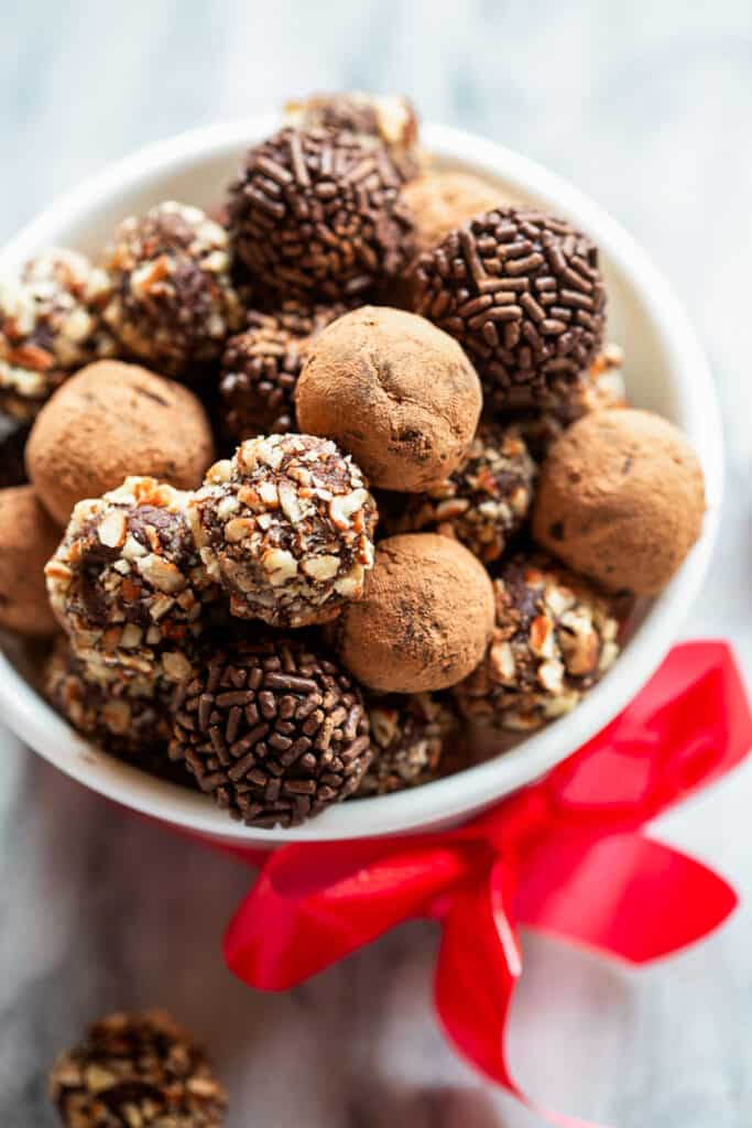 A variety of chocolate truffles homemade and in a white bowl with a red bow tied around it.