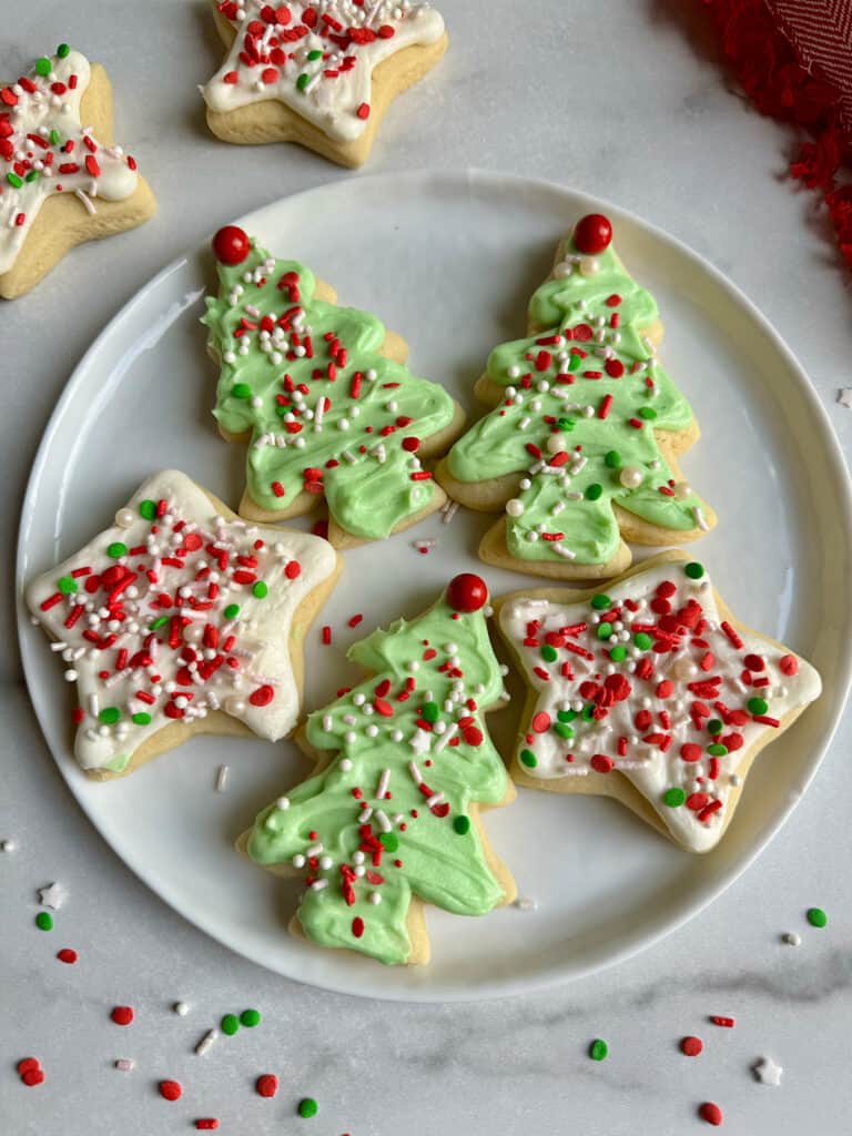A white plate with five Christmas frosted sugar cookies on it, three trees and two stars.