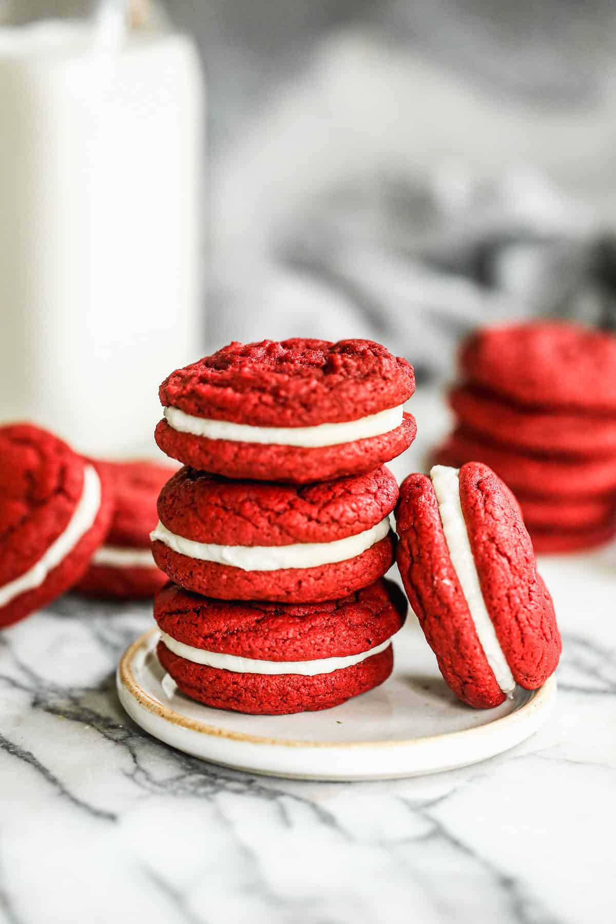 Three red velvet homemade Oreo cookies stacked on top of each other, with another one leaning against the stack.