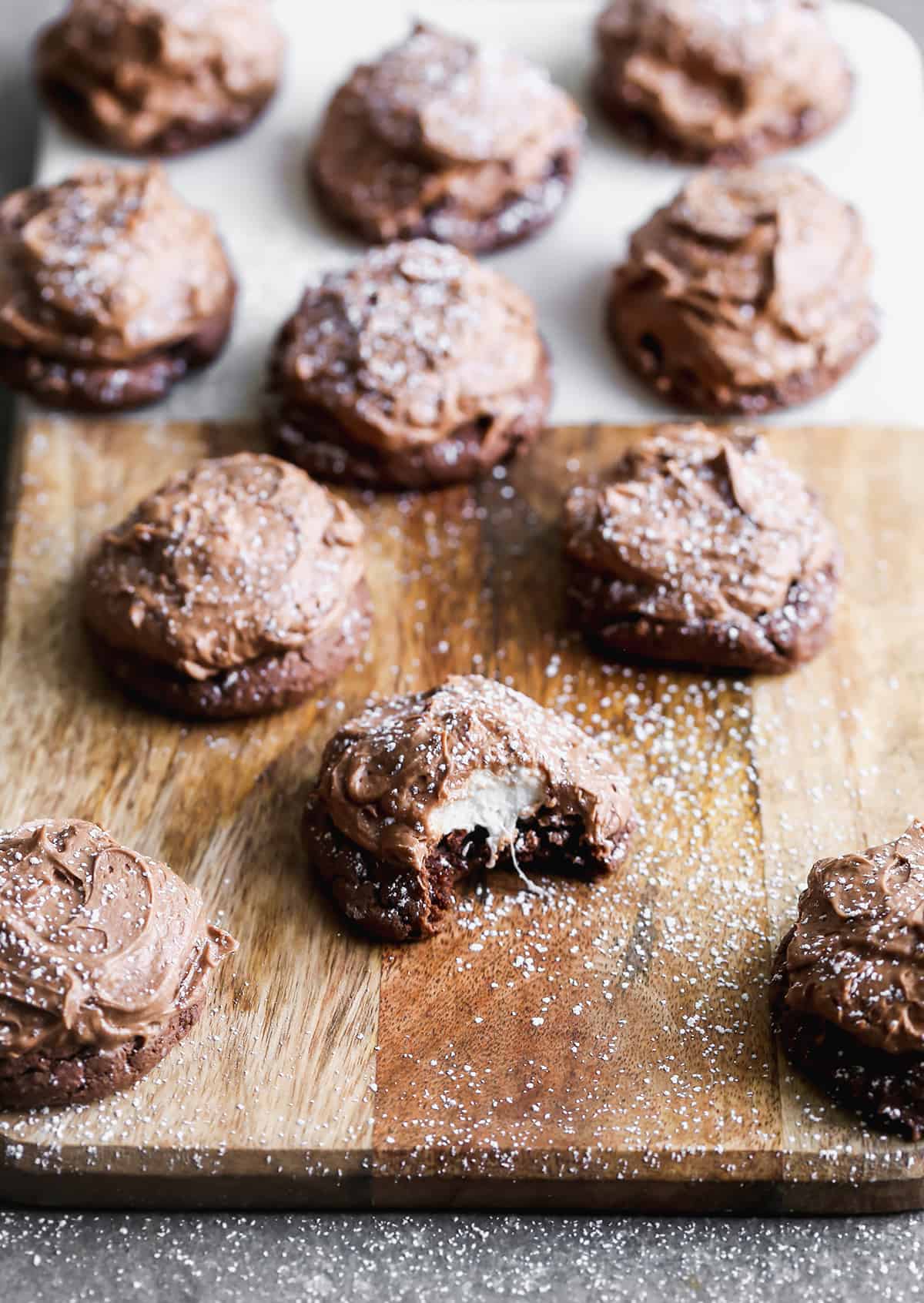 Chocolate Marshmallow Cookies on a wooden cutting board, dusted with powdered sugar with one bite taken out of one.
